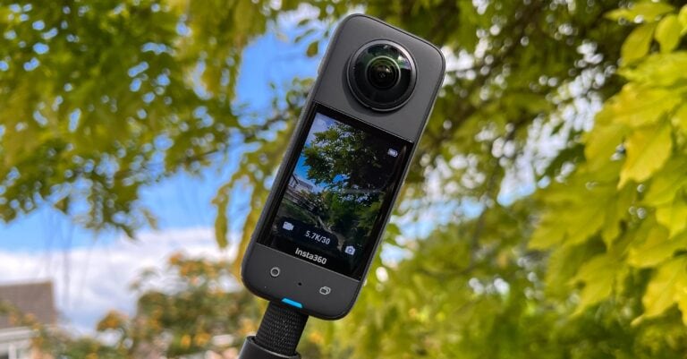 Detailní záběr na 360° kameru Insta360 umístěnou na černé tyči. Na displeji kamery je vidět živý náhled na stromy a budovy s údajem o natáčení v rozlišení 5.7K/30. Pozadí tvoří silně rozostřené zelené listy stromů proti modré obloze.