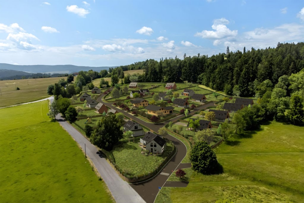 Letecký snímek vizualizace nové zástavby rodinných domů v šumavské krajině. Z ptačí perspektivy je vidět rozvržení parcel, nová příjezdová cesta a domy se sedlovými střechami, které jsou zasazeny do svahu. Lokalita je obklopena z jedné strany rozlehlými zelenými loukami a z druhé strany hustým jehličnatým lesem.
